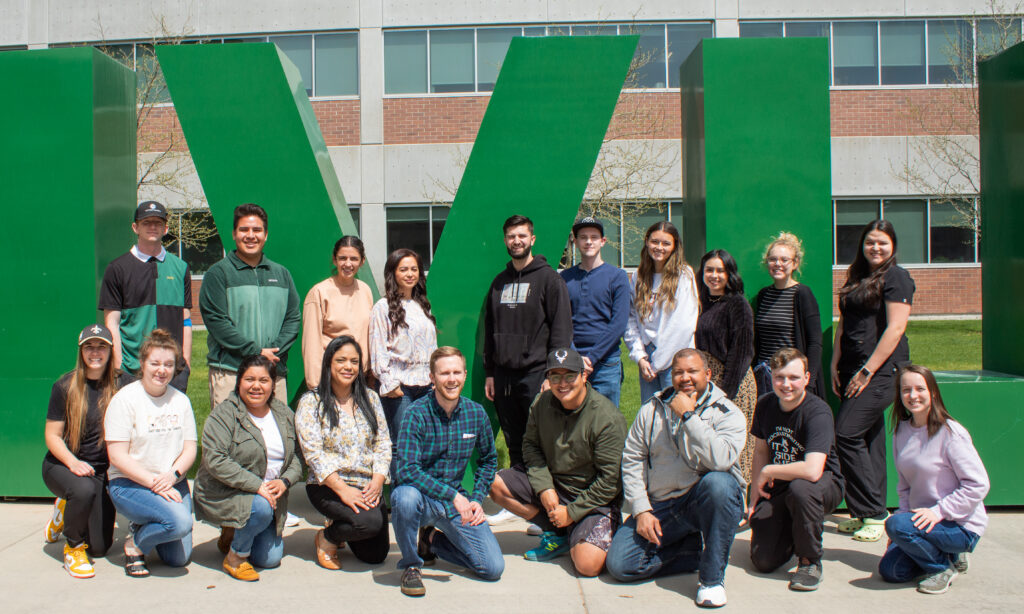 Photograph of Devin Gilbert and his Spanish translation students posing in front of the large UVU letters on campus